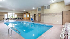 Una piscina con un bordeado de baldosas, sillas de descanso y una pequeña cabaña de madera.