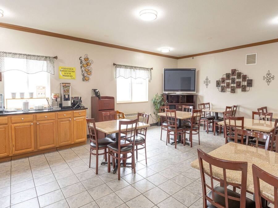 Comedor con mesas y sillas de madera, zona de cocina con armarios y una máquina de café, y un televisor en la pared.