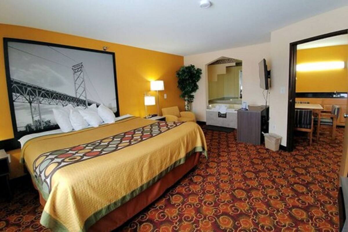 Quarto de hotel com cama, escrivaninha, cadeira, espelho, televisão e banheiro com banheira.