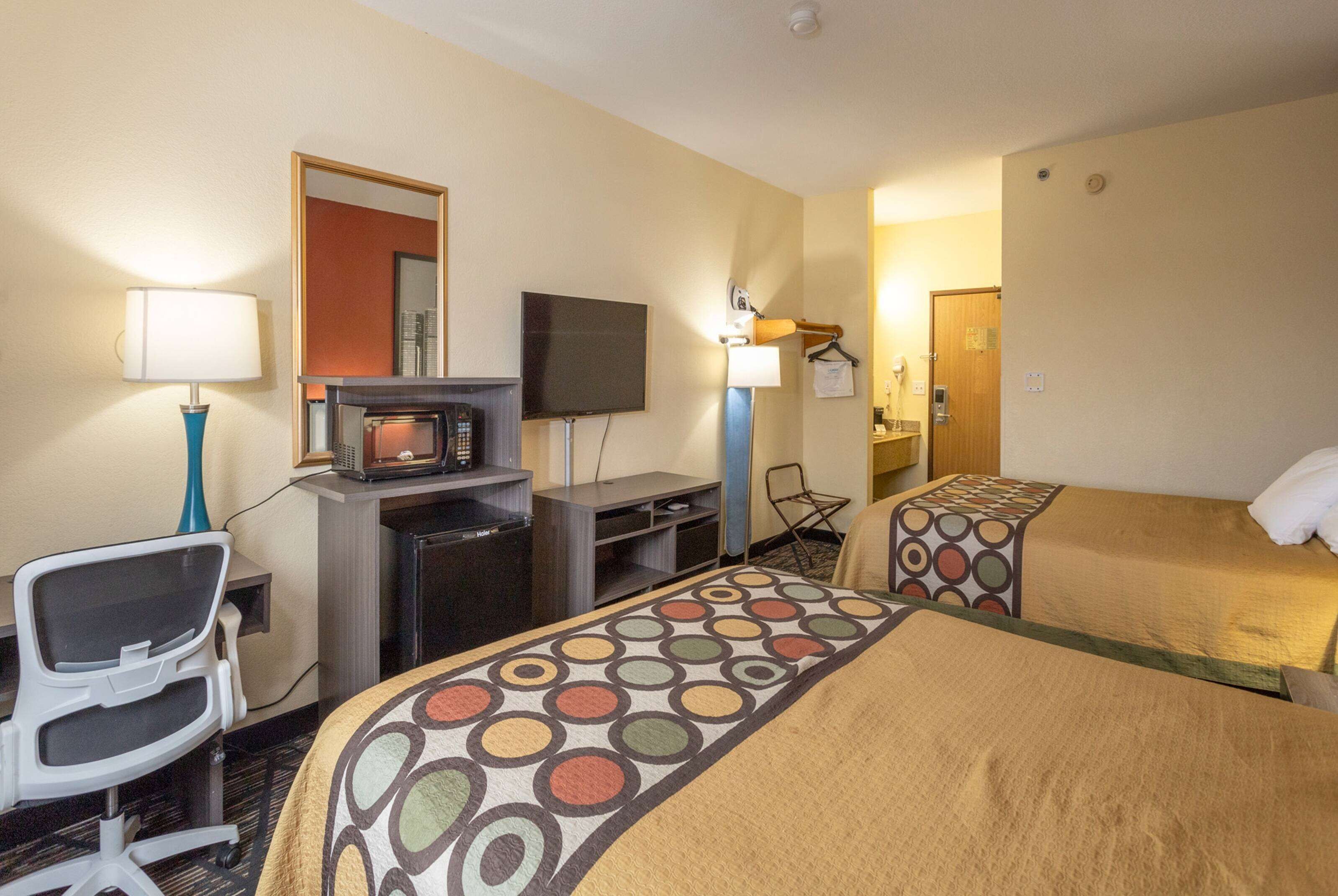 Une chambre d’hôtel avec deux lits, un bureau avec un ordinateur, une télévision et une chaise.