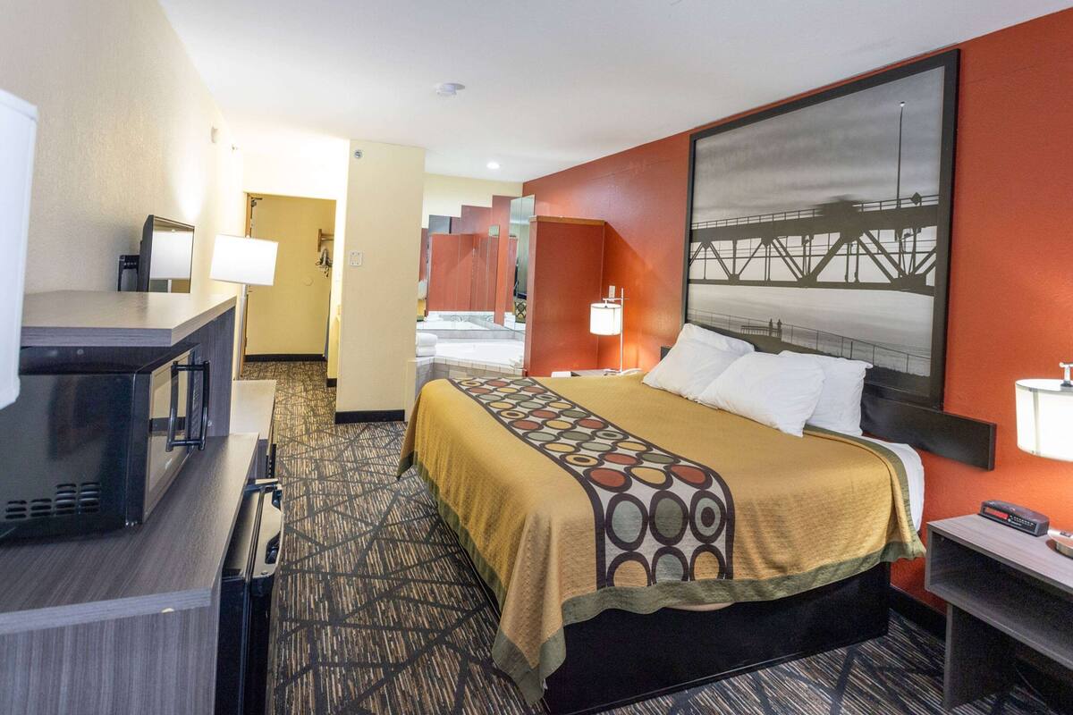 Quarto de hotel com uma cama, uma escrivaninha com candeeiro, micro-ondas e um quadro grande na parede.