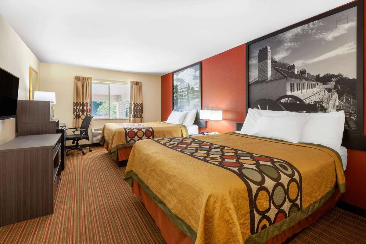 Quarto de hotel com duas camas, uma escrivaninha, televisão e uma janela grande.
