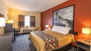 A hotel room with a large bed, a desk, a chair, a desk lamp, and a large framed picture on the wall.
