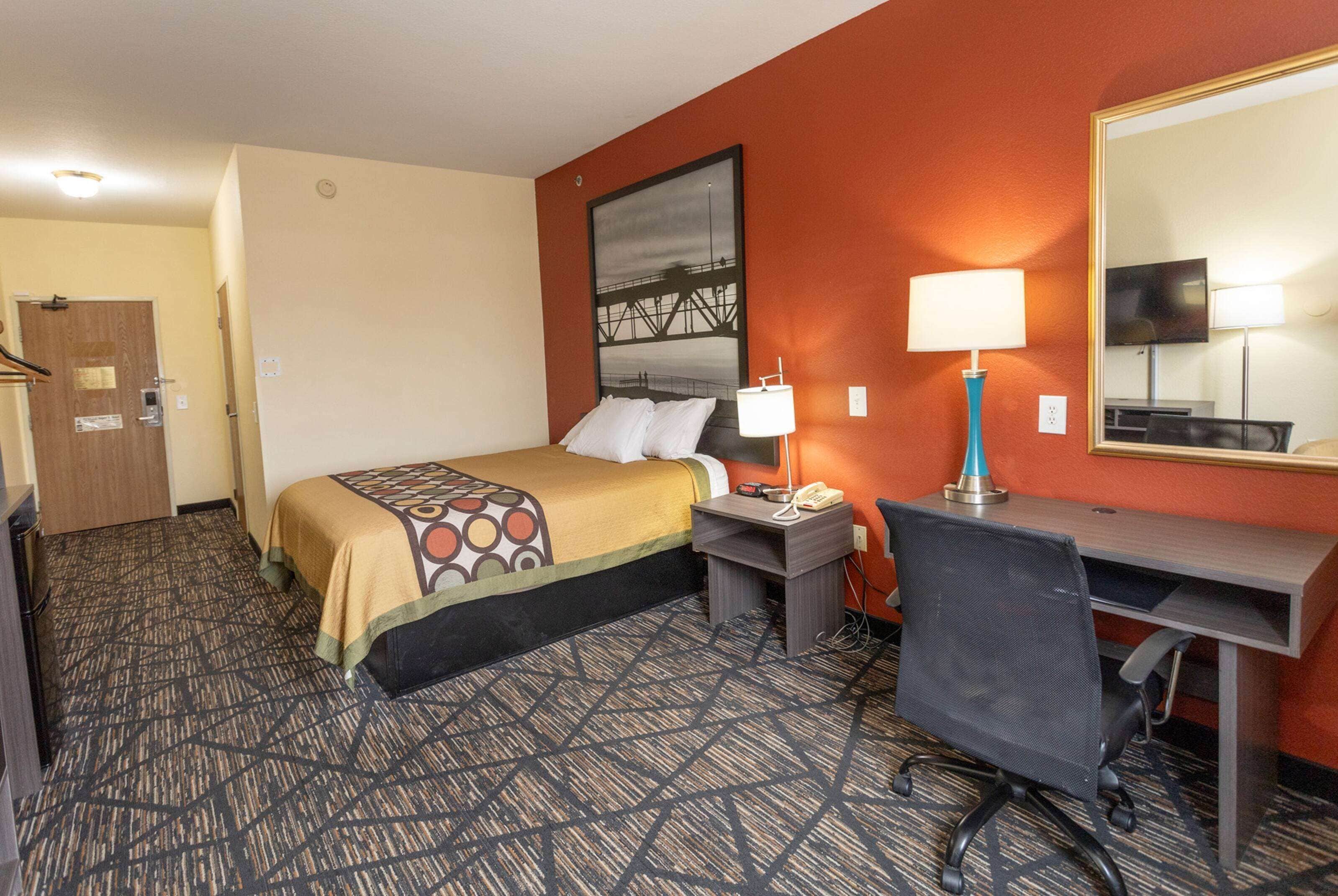 A hotel room with a bed, desk, chair, lamp, and a large mirror.