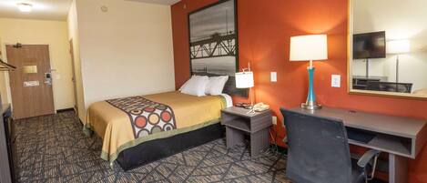 A hotel room with a bed, desk, chair, lamp, and a large mirror.