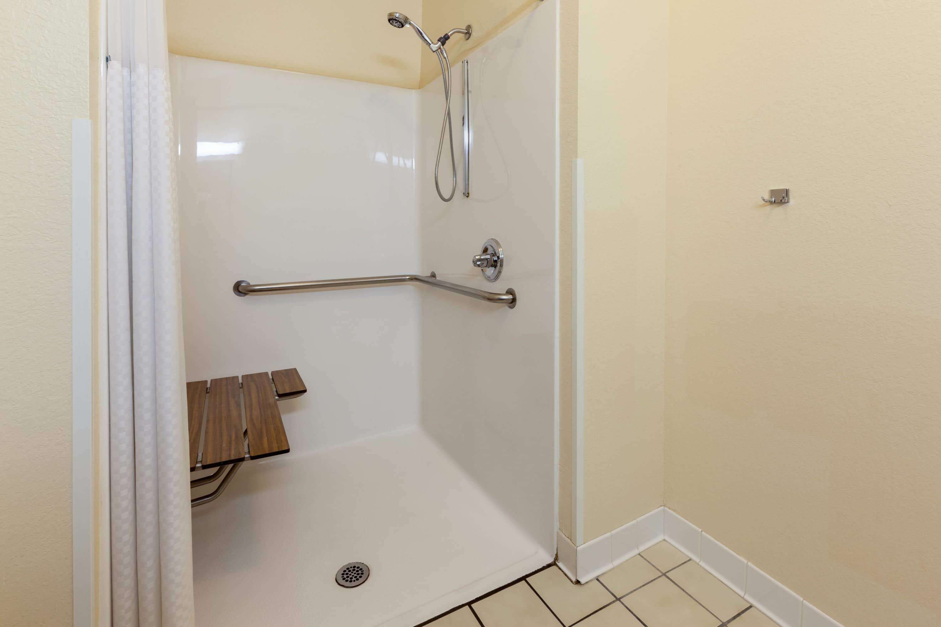 A shower area with a grab bar, a wooden bench, and a tiled floor.