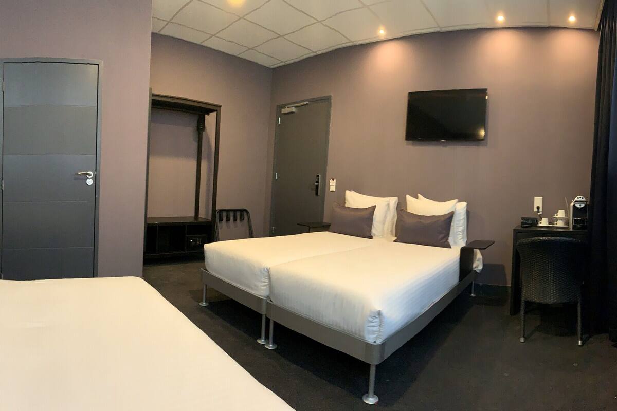 Habitación de hotel con dos camas, un escritorio, una silla, un televisor y una puerta.