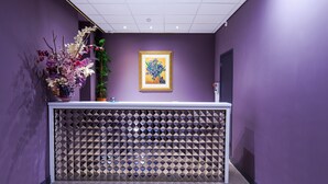 A reception area with a purple wall, a framed artwork, and a decorative plant. - Hotel De Looier (Amsterdam)