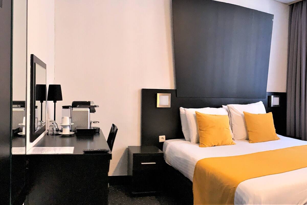 Habitación de hotel con cama, mesita de noche, lámpara y ventana con cortinas.