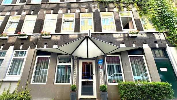 A hotel entrance with a modern design, featuring a large umbrella over the door, potted plants, and a sign indicating a hotel. - Hotel De Looier (Amsterdam)