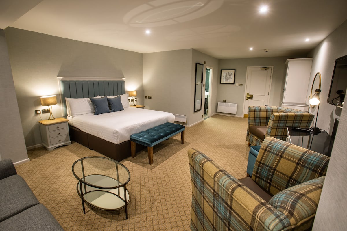 Quarto de hotel com uma cama, um banco, um sofá, uma mesinha e uma cadeira.