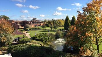 A golf course with a pond, surrounded by autumn foliage and a large building in the background.