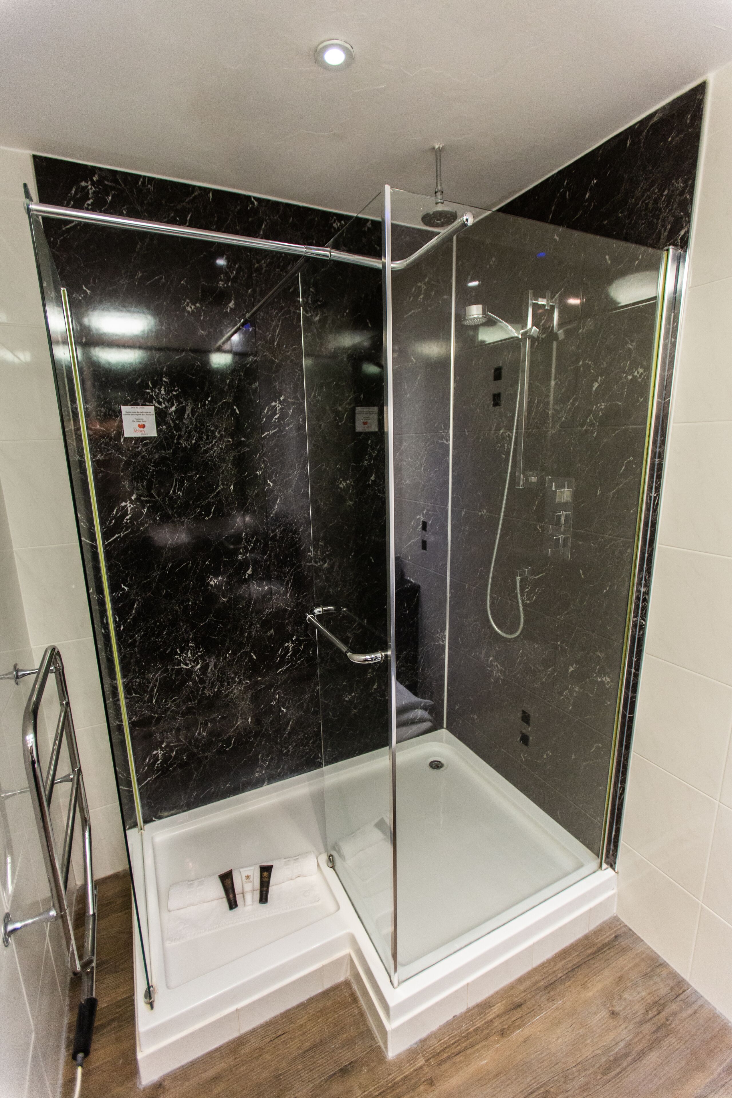 A modern shower enclosure with a glass door, a white base, and a black marble wall.