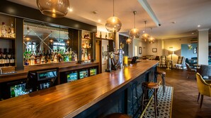A bar area with a wooden counter, multiple hanging pendant lights, and a variety of bottles and glasses. - The Abbey Hotel Golf & Spa  (Redditch)