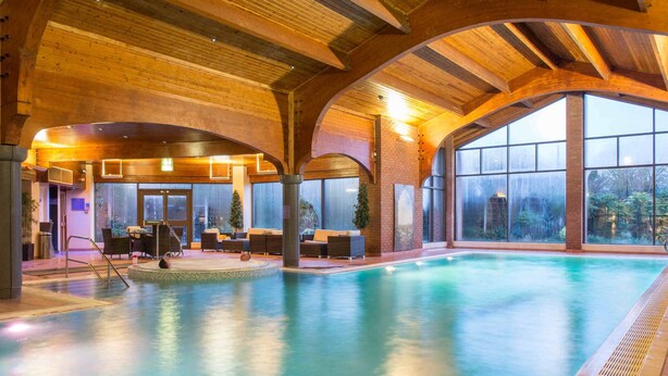 An indoor swimming pool with wooden beams, large windows, and seating areas. - The Abbey Hotel Golf & Spa  (Redditch)