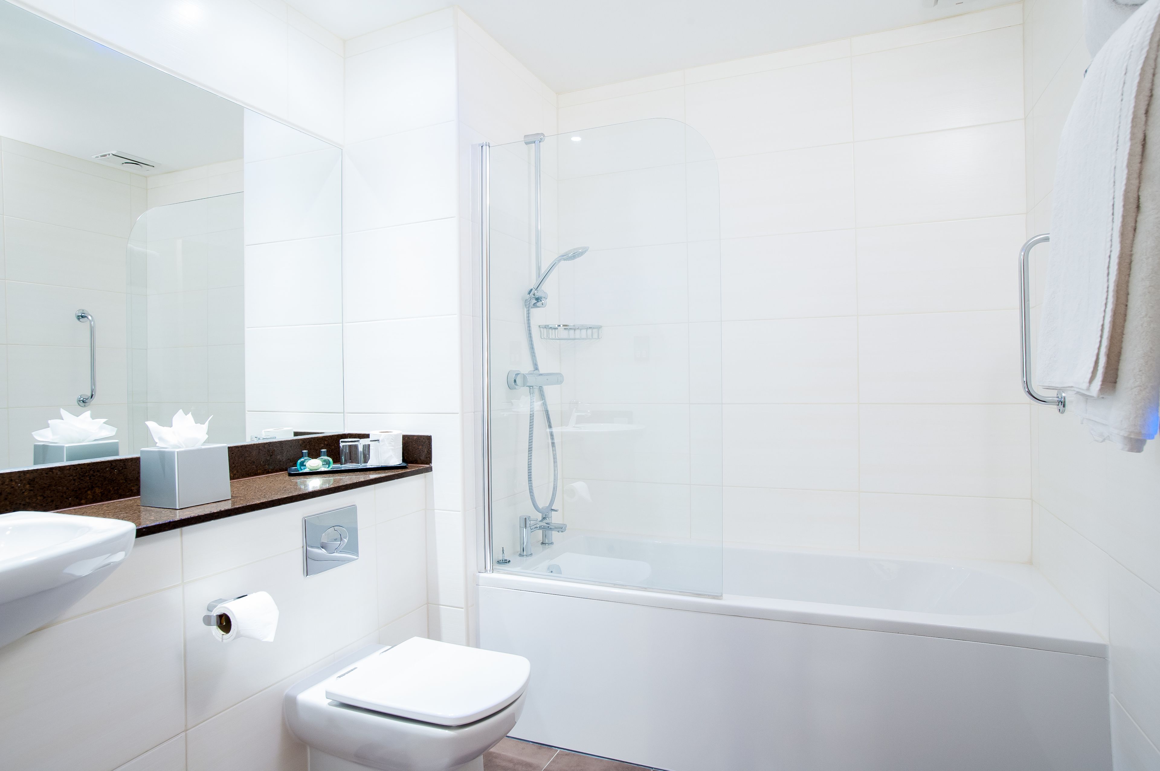 Un baño moderno con ducha de vidrio, inodoro blanco y lavabo con espejo superior.