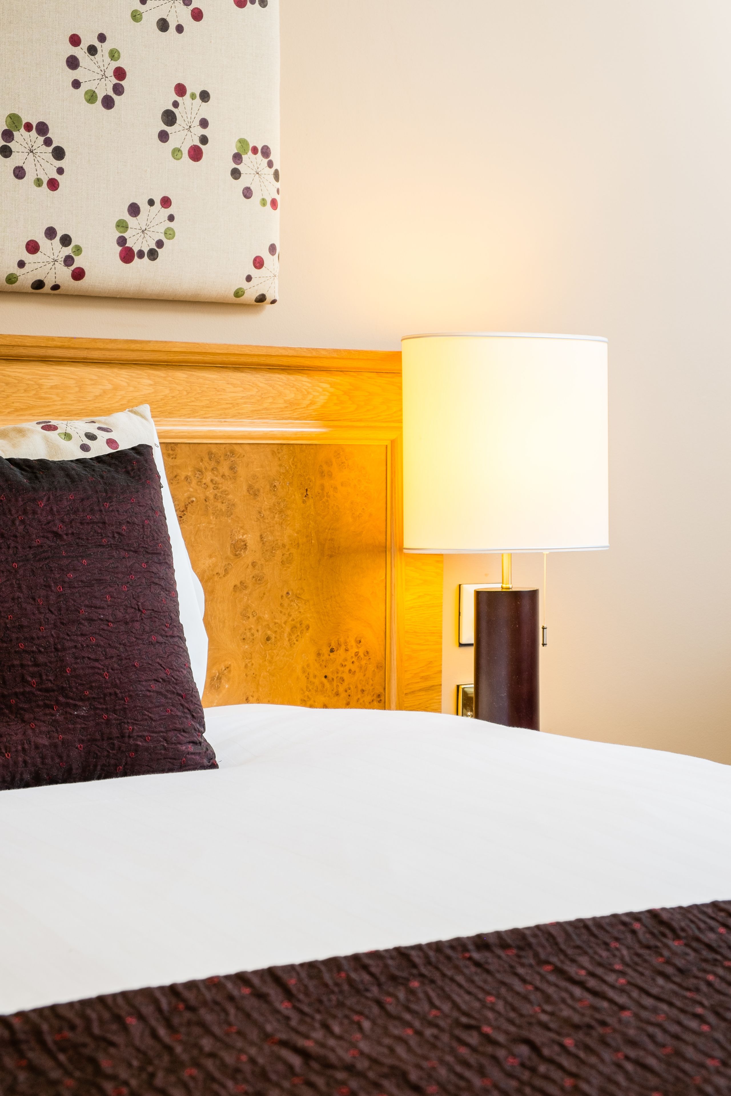 Una habitación de hotel con una cama bien hecha, una lámpara de noche y una obra de arte colgada en la pared.