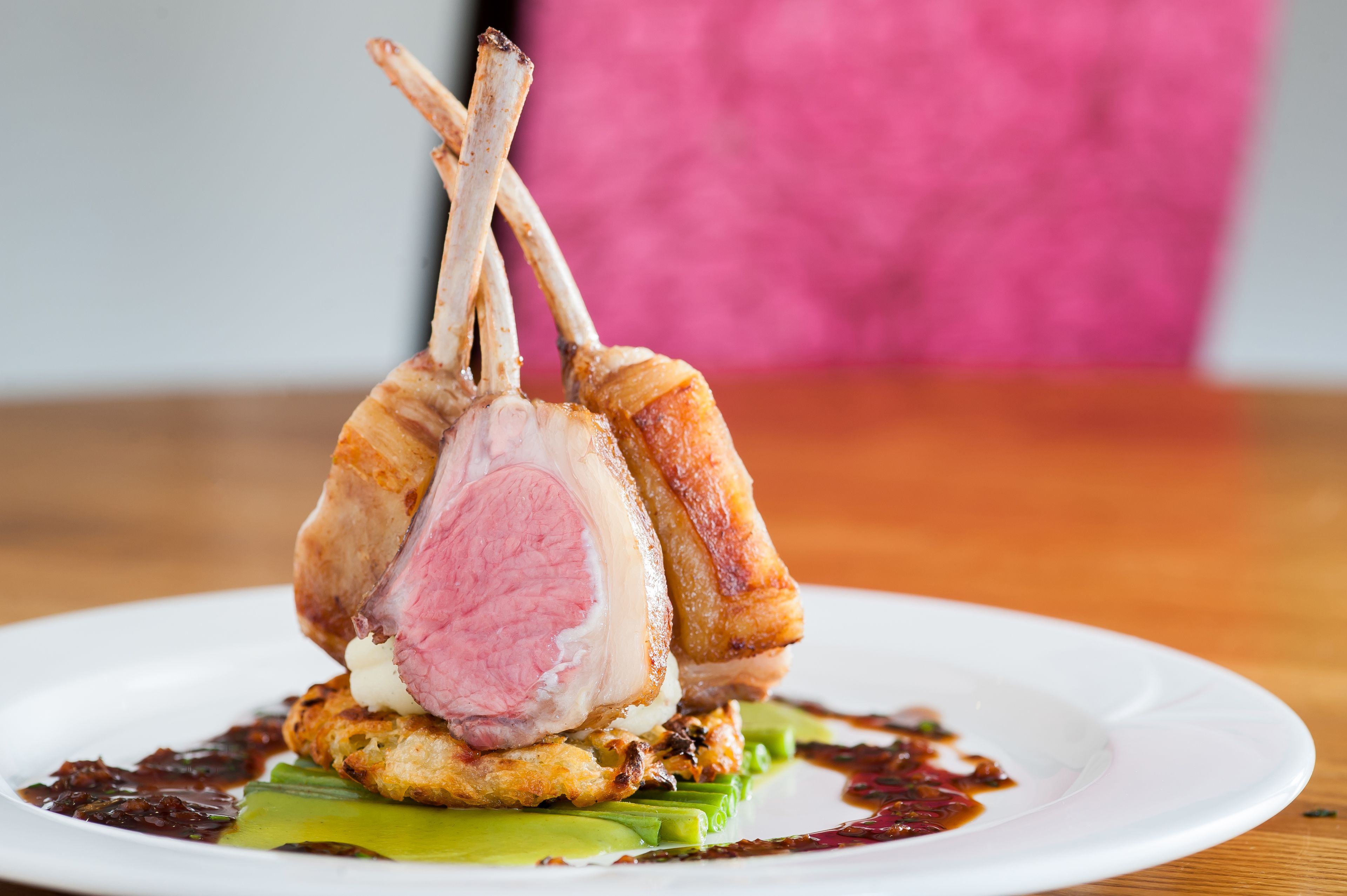Un plato con un asado de cordero, una rebanada de carne y un elemento crujiente sobre una cama de hojas verdes.