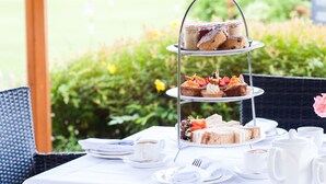 A three-tiered dessert stand with various pastries and sandwiches on a table set outdoors with a garden view. - The Abbey Hotel Golf & Spa  (Redditch)