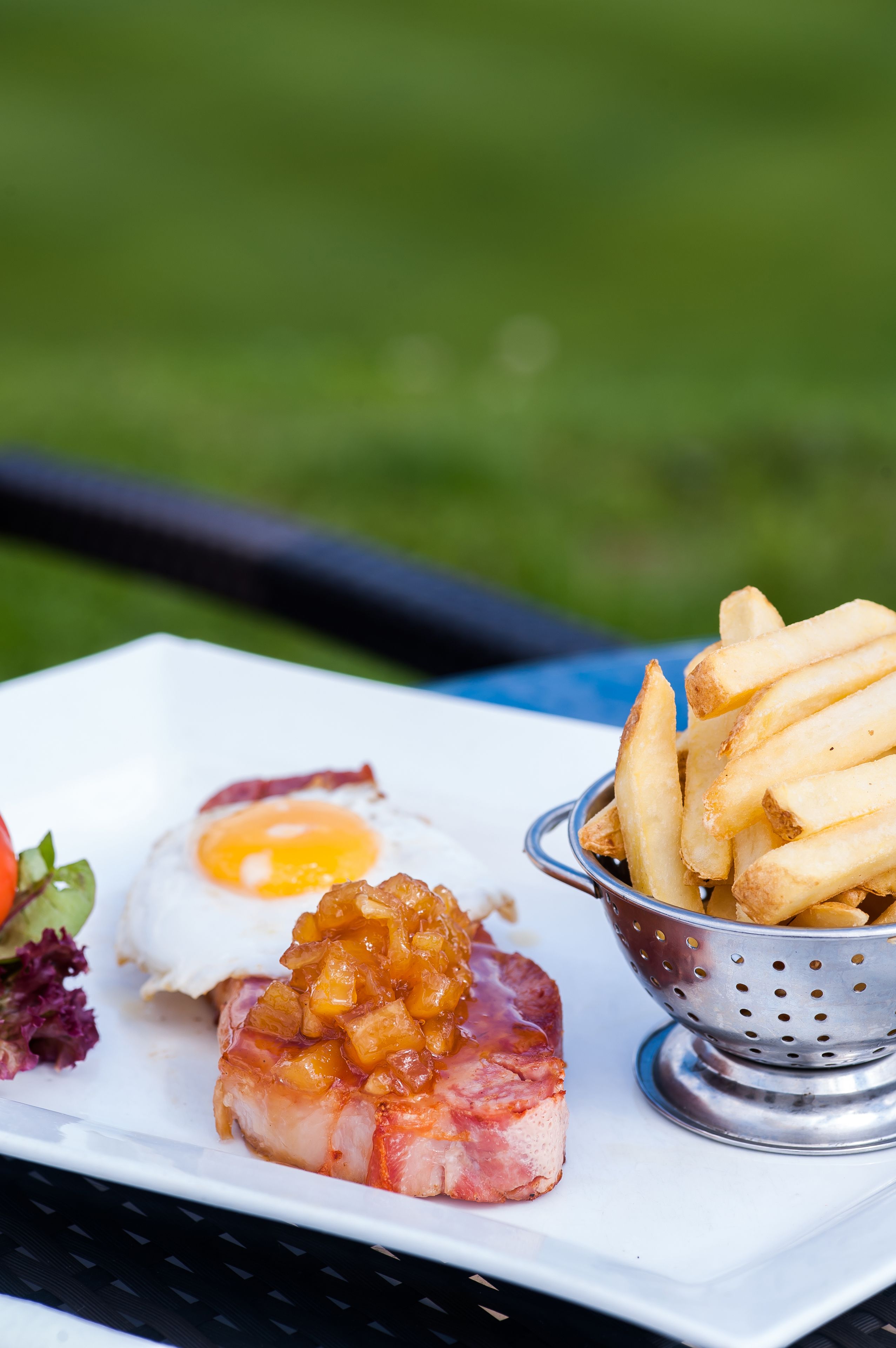 A plate with a ham slice topped with a fruit compote, a fried egg, and a side of fries.