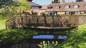 A residential building with a pond, wooden bridge, and daffodils in the foreground. - The Abbey Hotel Golf & Spa  (Redditch)