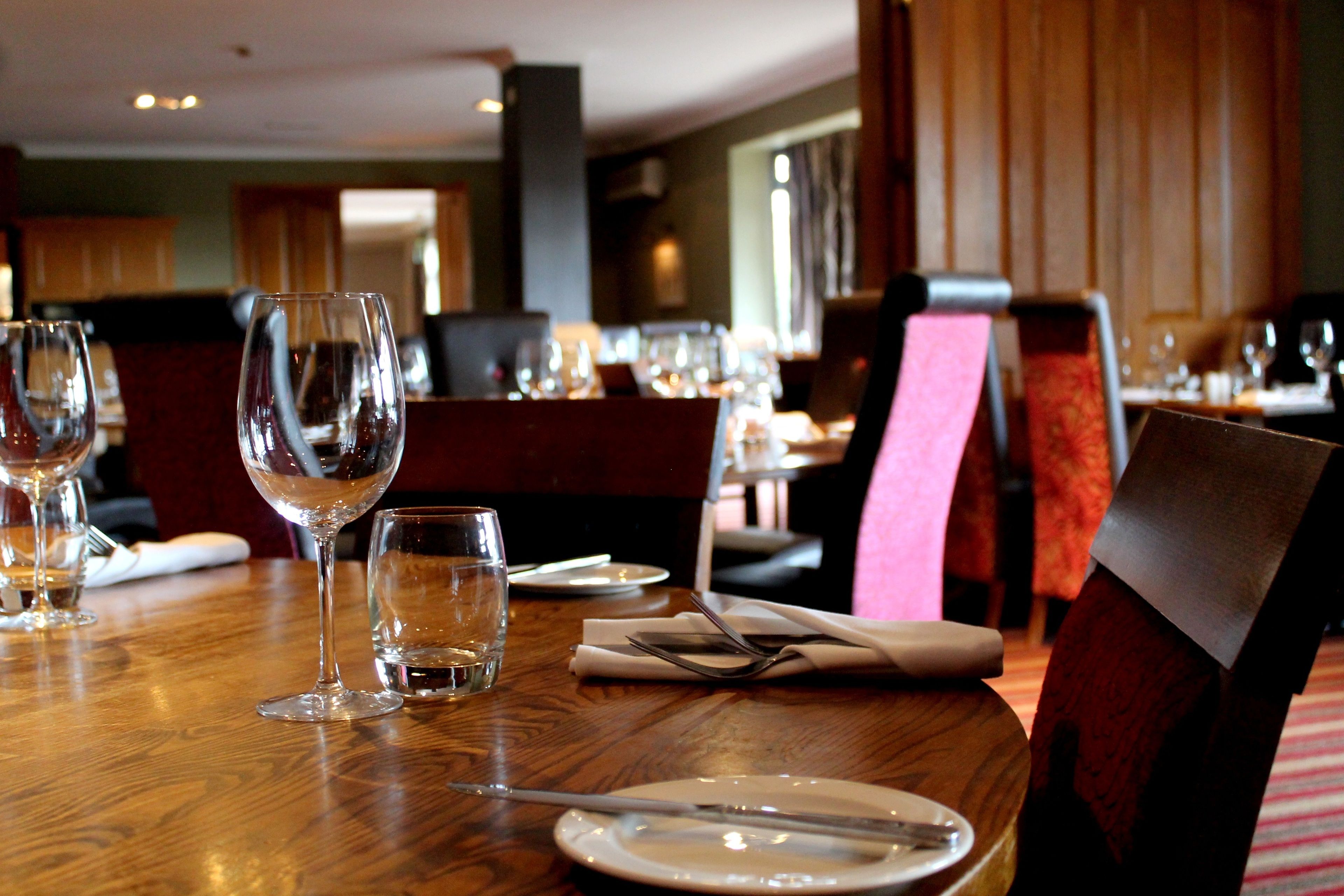 A dining table set with plates, cutlery, and wine glasses in a restaurant with wooden furniture and a red upholstered chair.