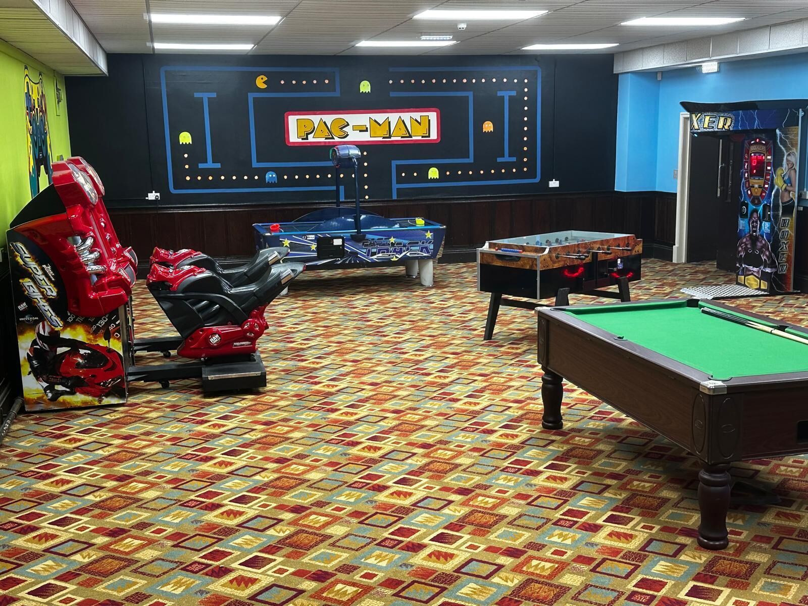A room with a pool table, foosball table, and a Pac-Man arcade game.