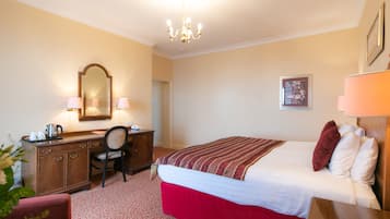 Een hotelkamer met een bed, een bureau, een stoel, een kast, een spiegel, een kroonluchter en een ingelijst kunstwerk aan de muur.
