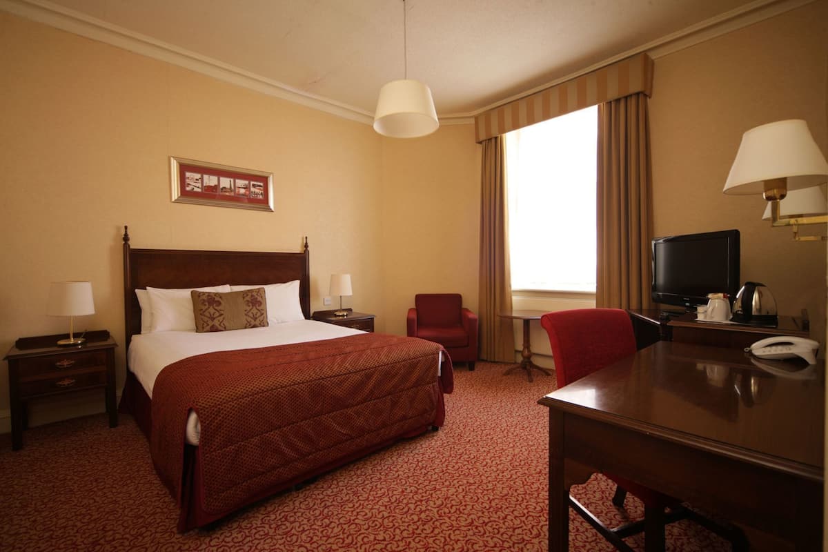 A hotel room with a large bed, a desk with a chair, a television, and a window with curtains.