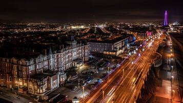 Un paisaje urbano nocturno con edificios iluminados, una torre destacada y una calle concurrida con estelas de luz.