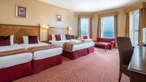 A hotel room with three beds, a sofa, a desk, and a large window offering a view. - The Imperial Hotel (Blackpool)