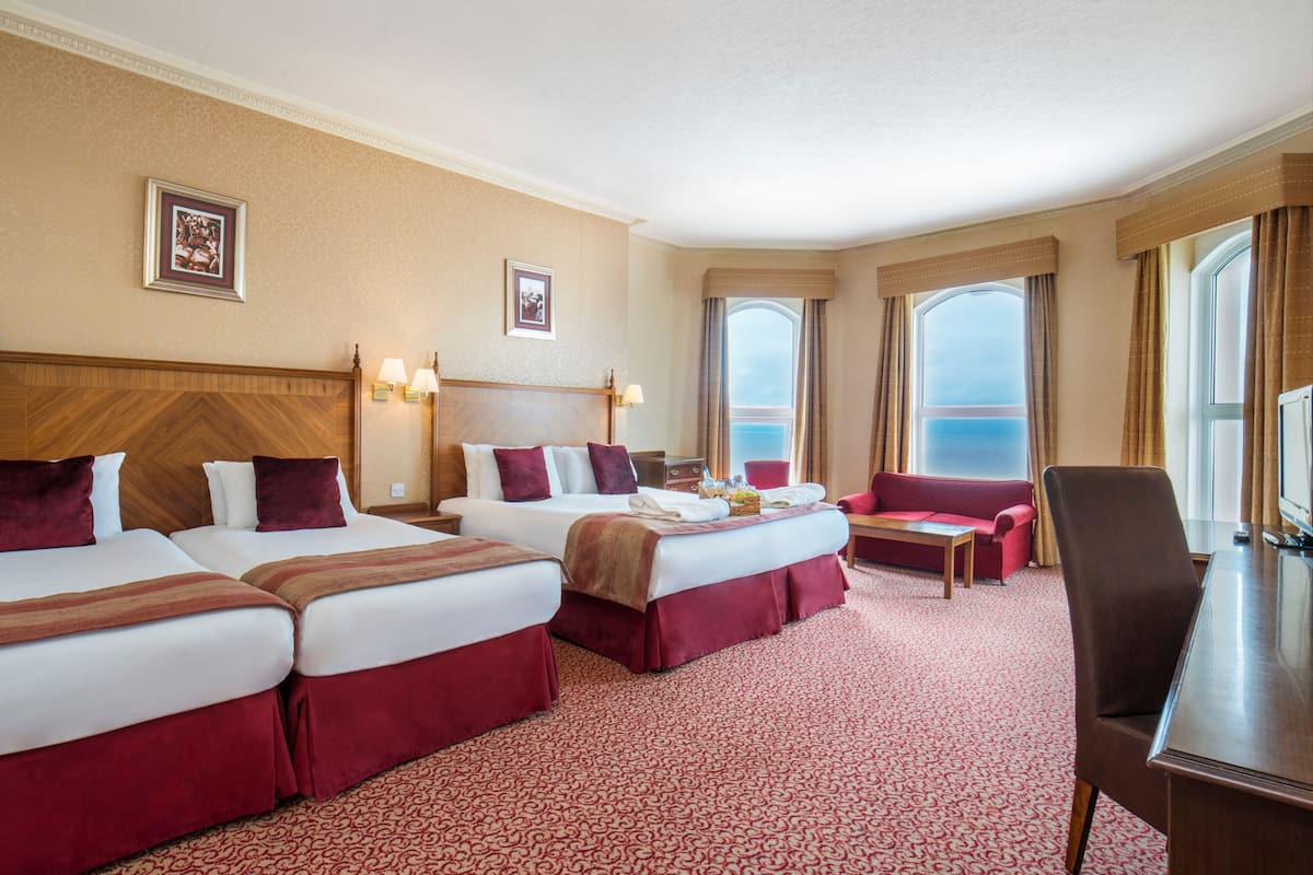 A hotel room with three beds, a sofa, a desk, and a large window offering a view.