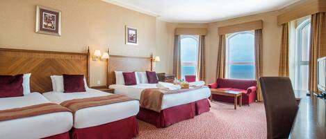 Habitación de hotel con tres camas, un sofá, un escritorio y un ventanal con vistas.