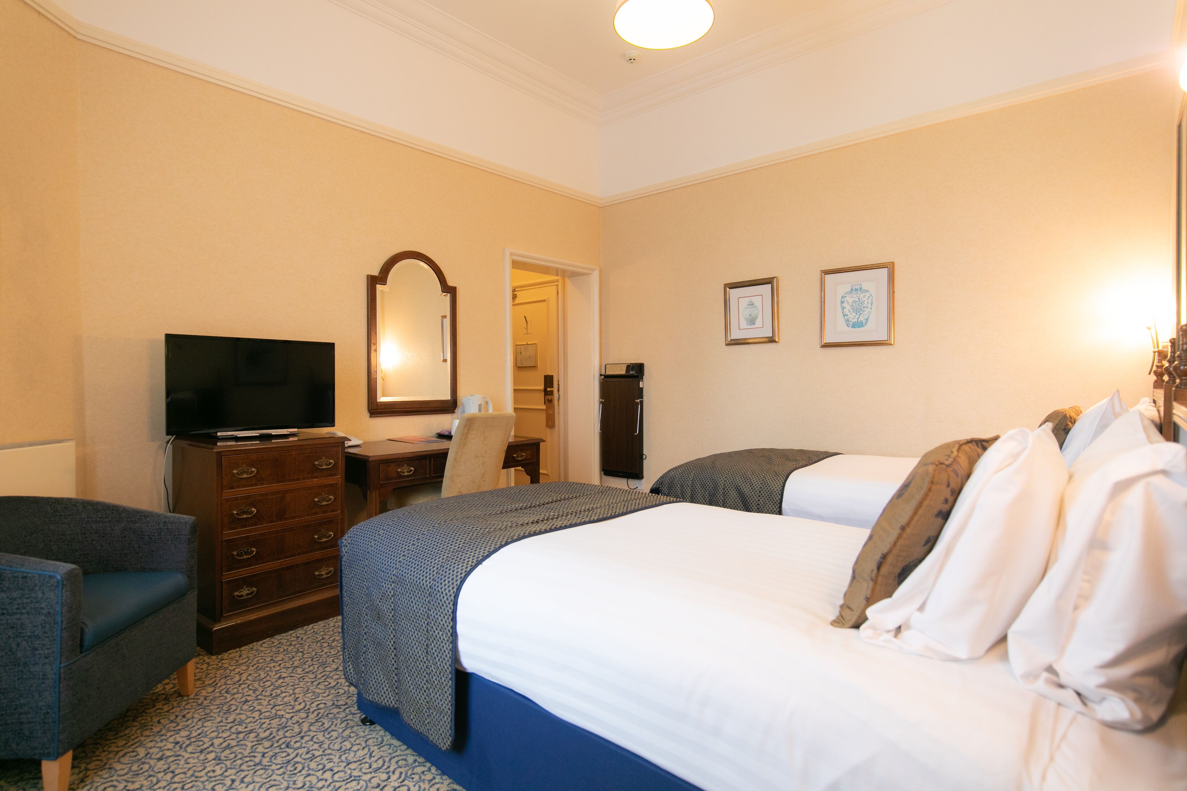 A hotel room with a large bed, a dresser, a television, and a desk with a chair.