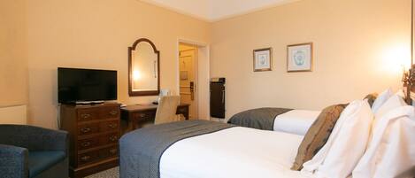 A hotel room with a large bed, a dresser, a television, and a desk with a chair.