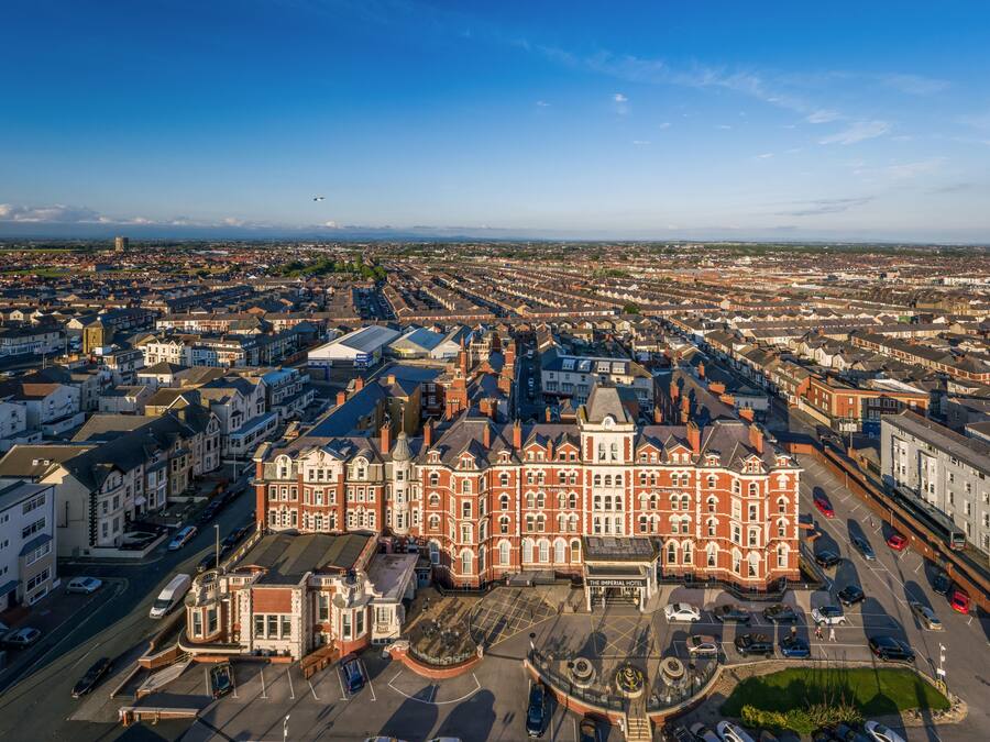 An aerial view of a cityscape with The Imperial Hotel prominently featured in the foreground, surrounded by a mix of residential and commercial buildings.