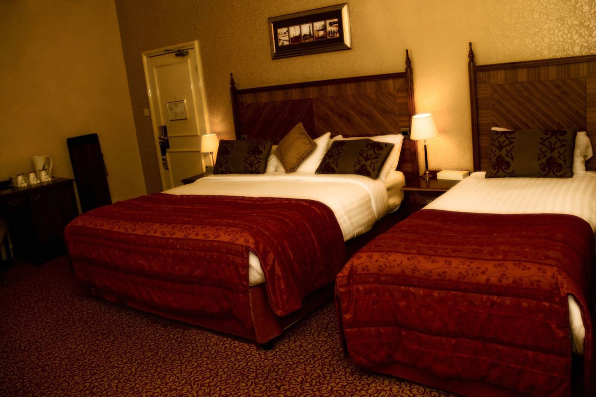 A hotel room with two beds, a nightstand with a lamp, a dresser, and a framed picture on the wall.