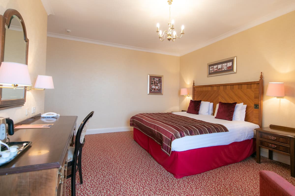 A hotel room with a bed, bedside table, lamp, chair, desk, and a mirror.