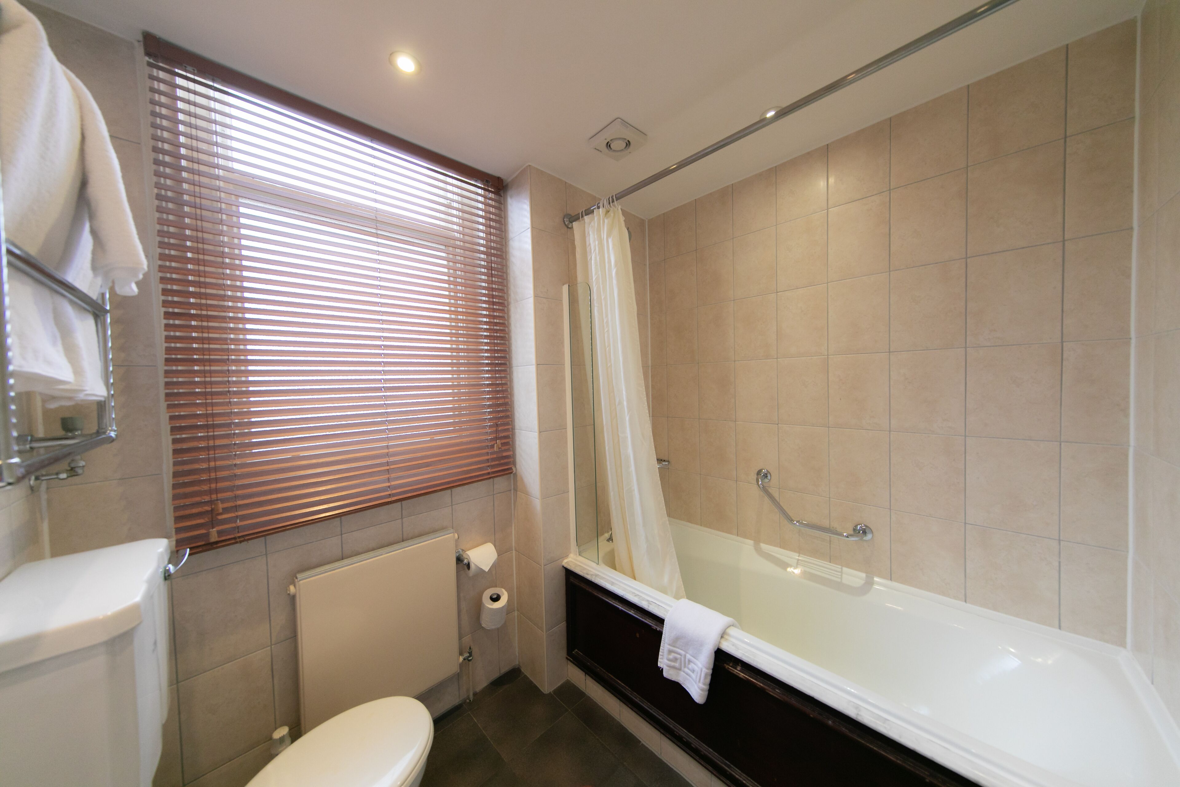 A bathroom with a bathtub, toilet, and window with blinds.