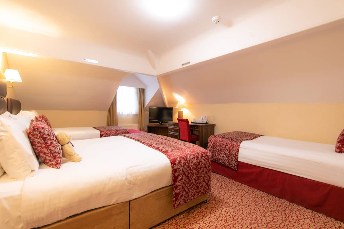 A hotel room with two beds, a desk, a television, and a lamp.