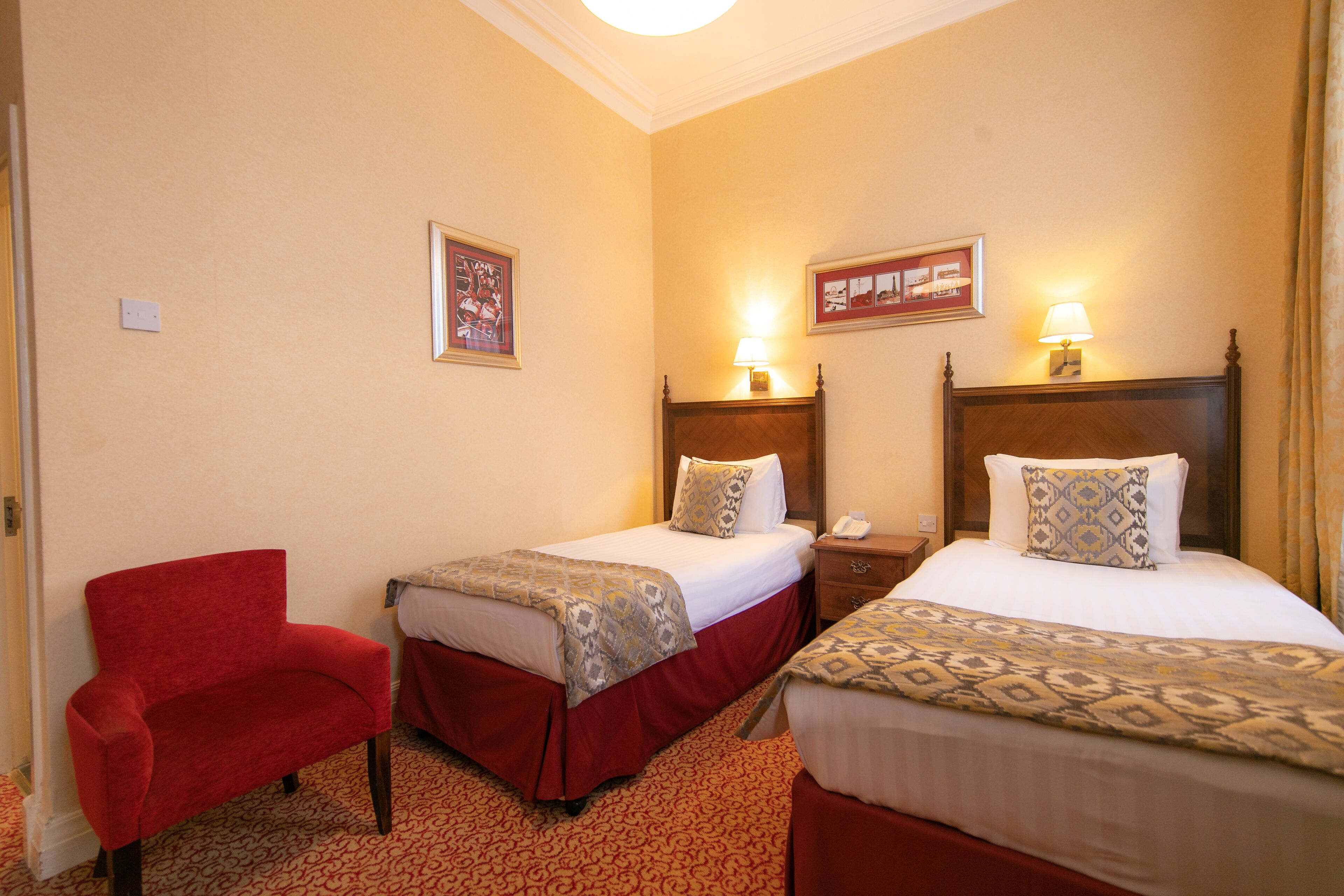 A hotel room with two beds, a red armchair, and a wooden headboard.