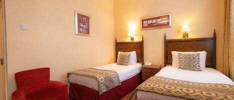 A hotel room with two beds, a red armchair, and a wooden headboard.