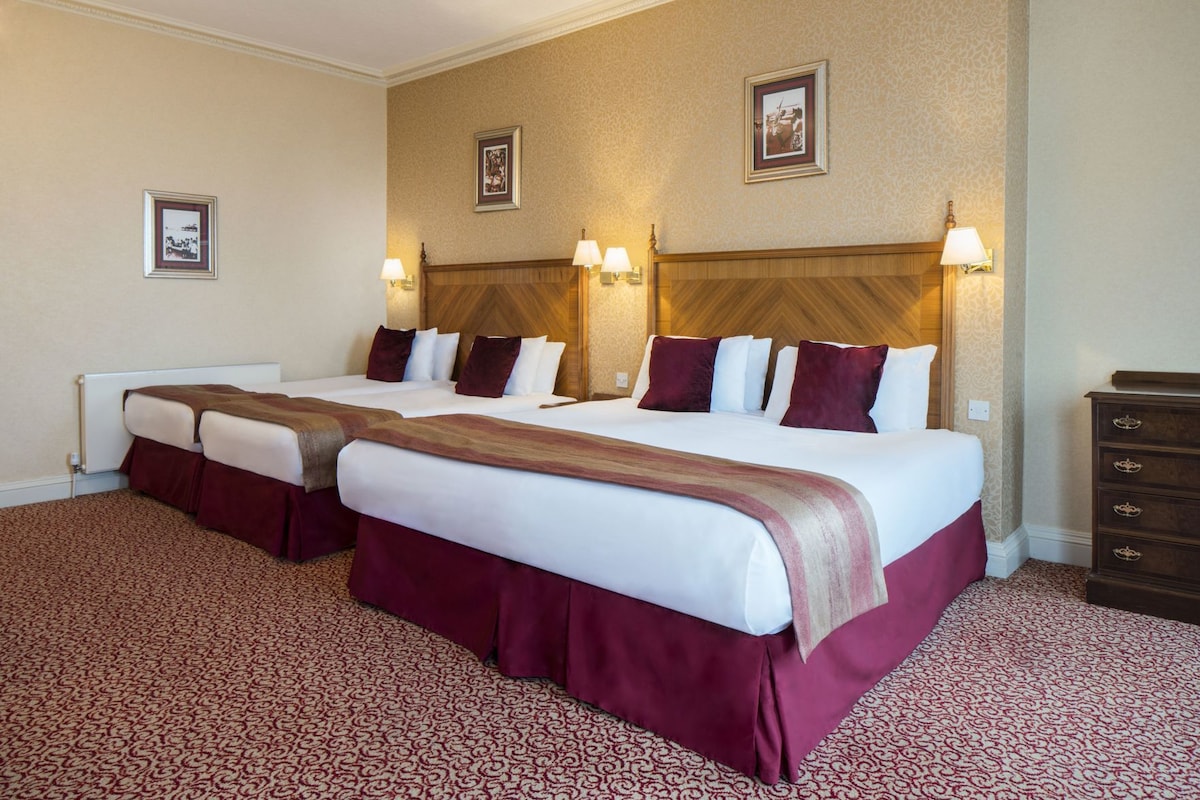 A hotel room with two beds, a wooden headboard, a patterned carpet, and a dresser.