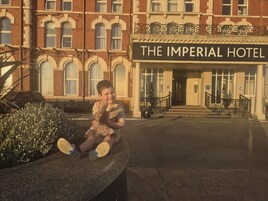 Een kind zit op een stenen bank voor Hotel The Imperial.