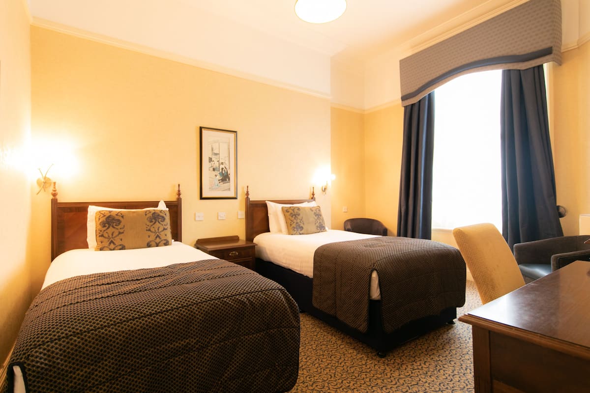 A hotel room with two beds, a desk, a chair, and a window with curtains.