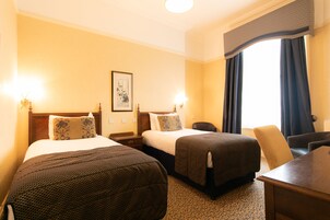 Een hotelkamer met twee bedden, een bureau, een stoel en een raam met gordijnen.