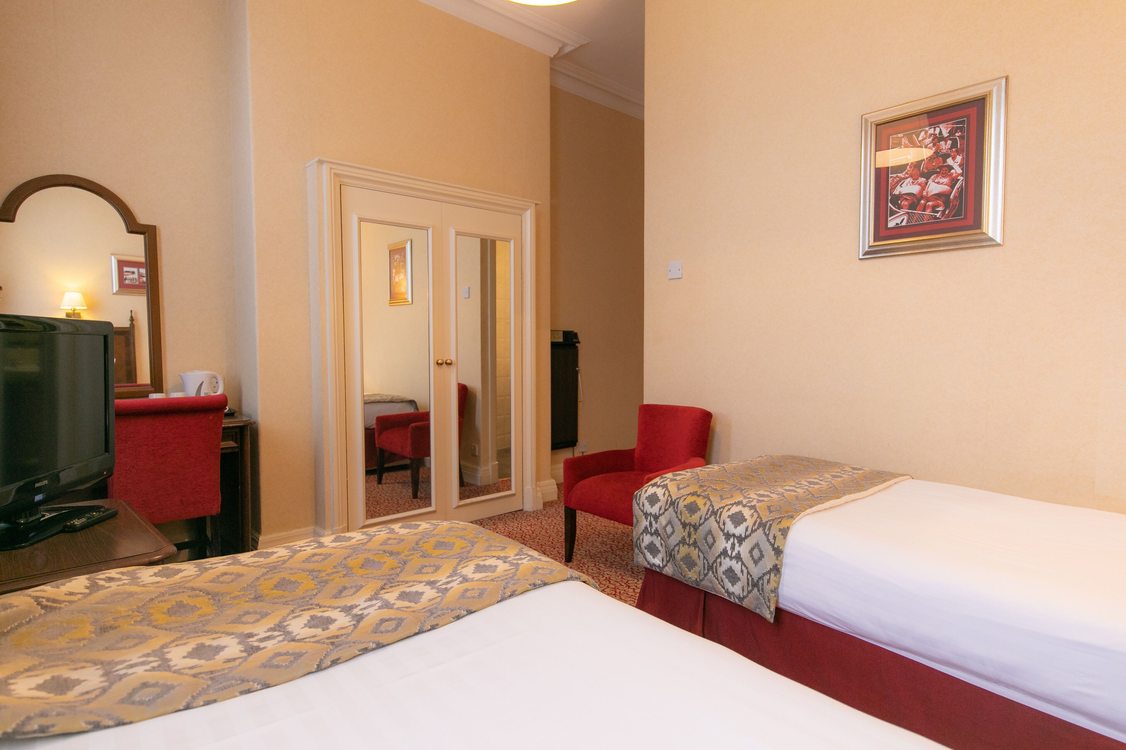 Habitación de hotel con dos camas, un televisor, un espejo y una silla roja.
