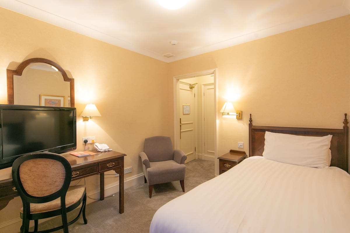 A hotel room with a bed, a desk with a chair, a television, and a mirror.