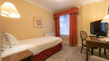 A hotel room with a single bed, a desk with a computer, a chair, and a window with curtains.