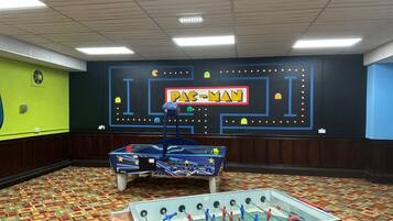 A room with a foosball table, a Pac-Man themed wall, and a patterned carpet.